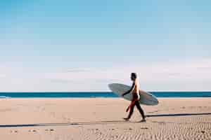 無料写真 ウェットスーツを着た孤独なサーファーがサーフボードで海または海岸に向かって歩くオープンで空のビーチ