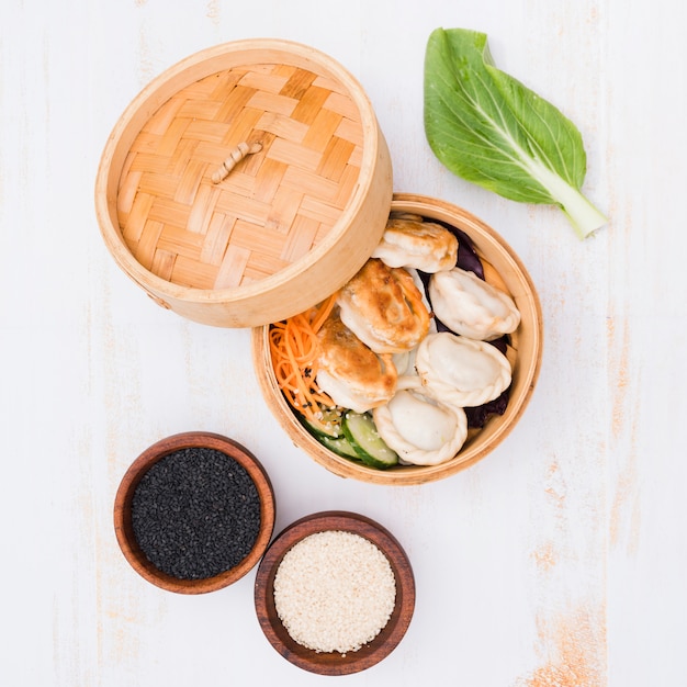 Free photo an open bamboo steamers with dumplings and sesame seeds on textured backdrop