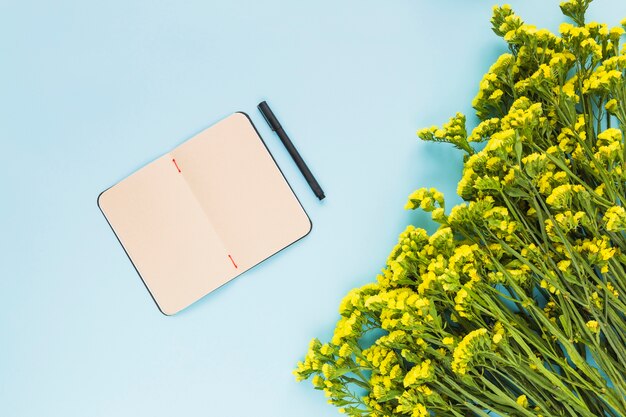 An open blank diary with pen and yellow flowers on blue background