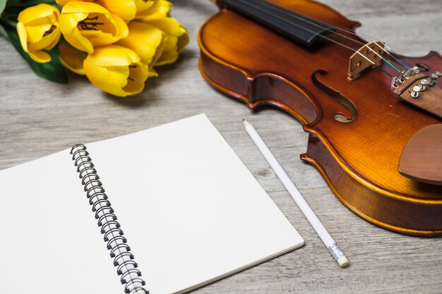 An open blank notebook; pencil; tulip and classical violin on plank backdrop