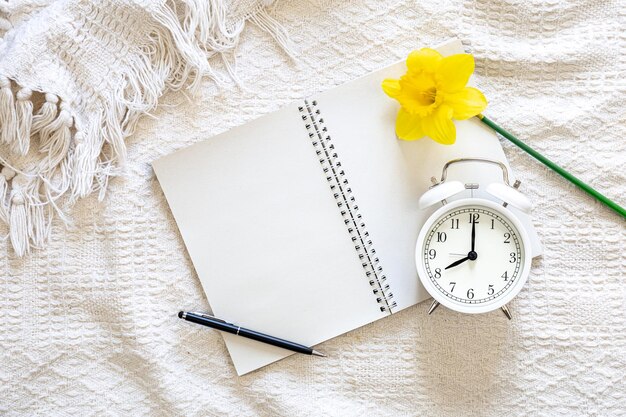 Free photo open blank notebook yellow flower and white alarm clock in white bed top view