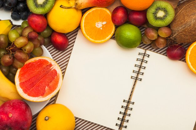 An open blank spiral notepad with many fresh fruits