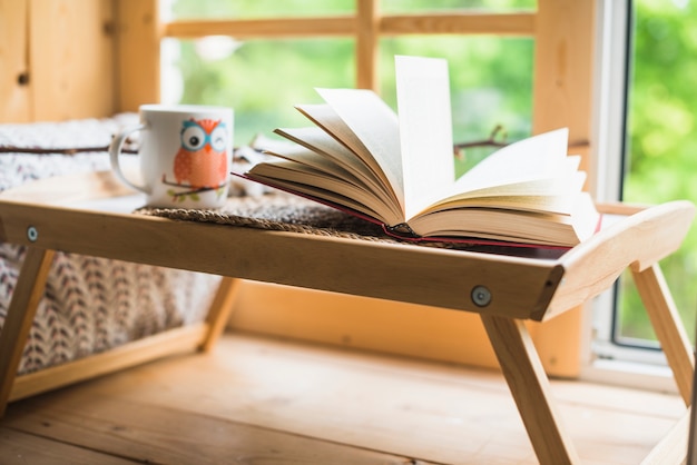 Open book and coffee cup on table near window