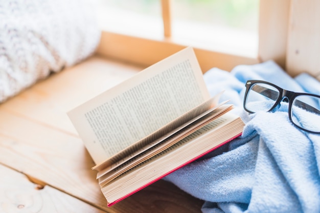 Открытая книга и очки на синем одеяле над столом