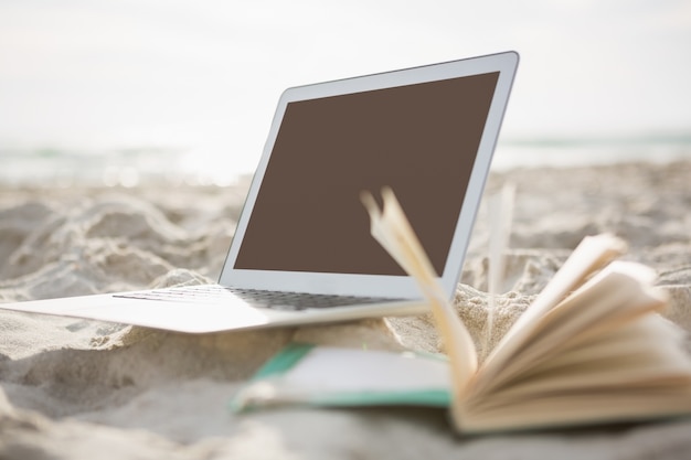 Open book and laptop on sand