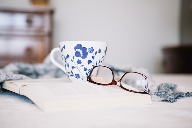 Foto gratuita apra il libro con la tazza e gli occhiali