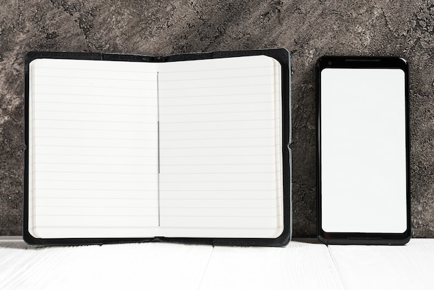 An open diary and mobile phone showing white screen on desk against wall