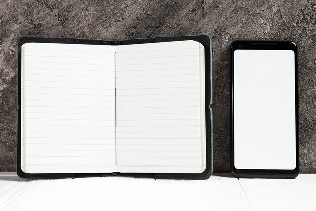 開いている日記と壁に机の上の白い画面を示す携帯電話