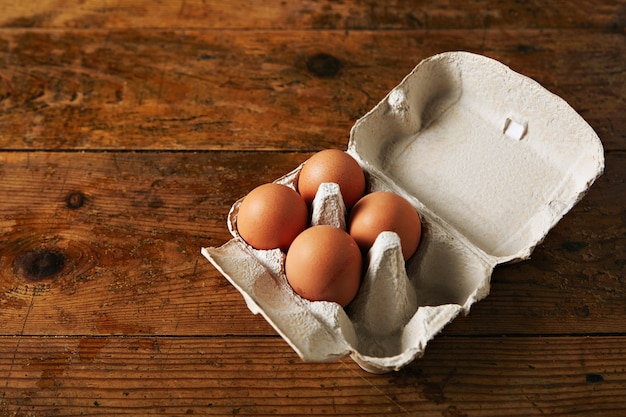 Free photo open egg carton for six eggs containing four brown eggs on a rough rustic brown wooden table