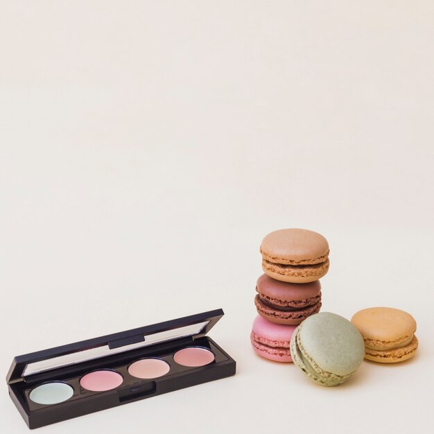 An open eye shadow palette with macaroons on beige background