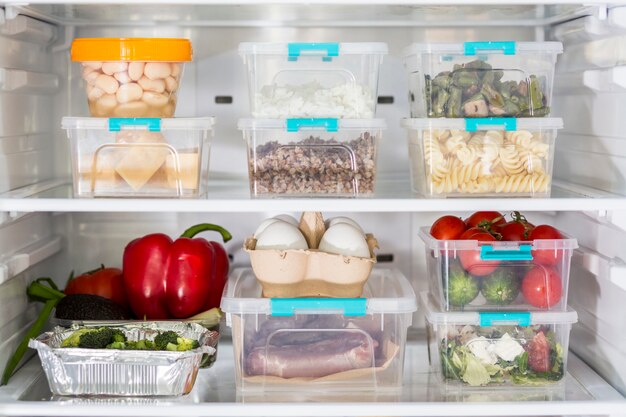 Open fridge with plastic food containers and vegetables