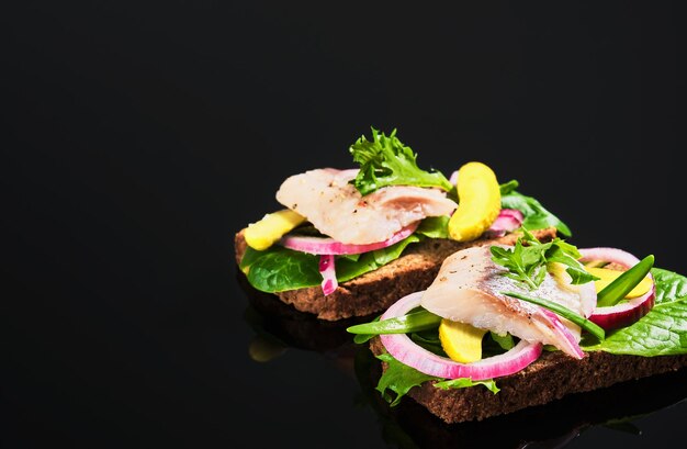 Open herring sandwich - traditional Danish smorrebrod. Sandwiches are located on a dark background. Close-up, shallow depth of field.