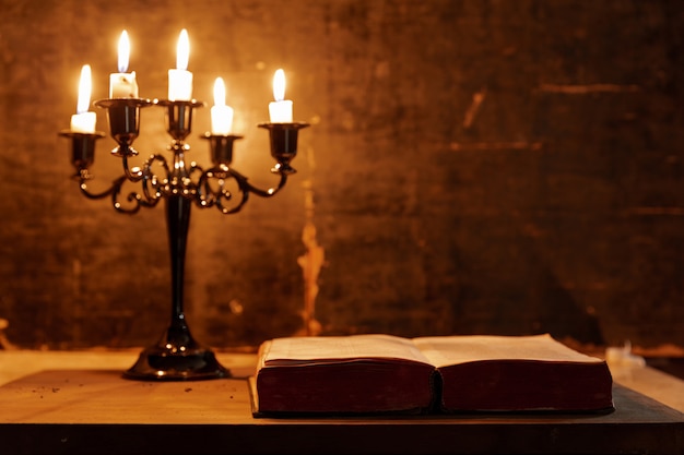 Open Holy Bible and candle on a old oak wooden table. Beautiful gold background. Religion concept. 