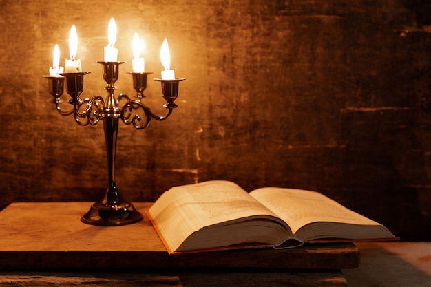 Open Holy Bible and candle on a old oak wooden table. Beautiful gold background. Religion concept. 