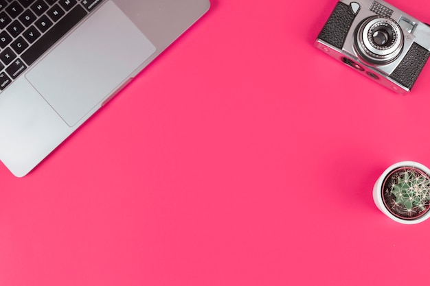 An open laptop; camera and cactus potted plant on pink background