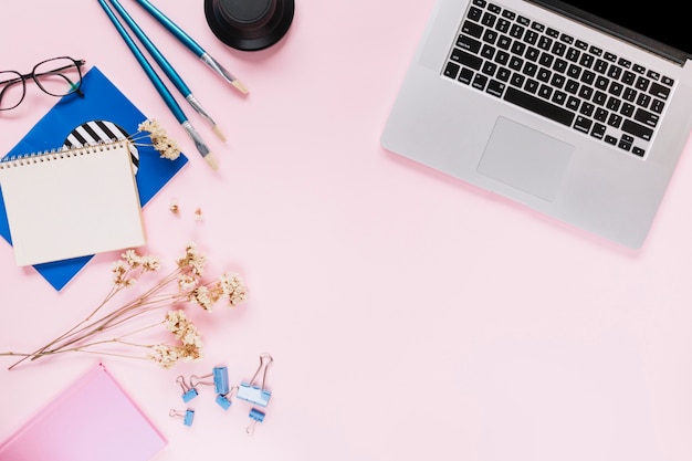 An open laptop; flowers and stationery on pink background