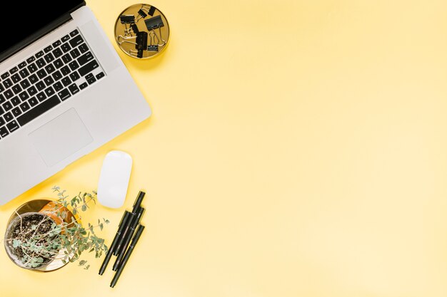 An open laptop; mouse with bulldog paper clips and felt-tip pens on yellow background