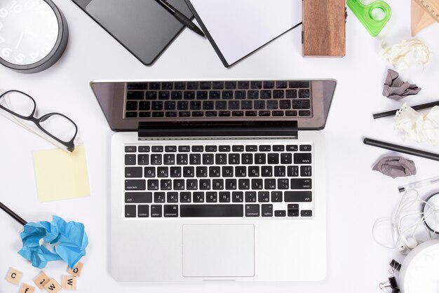 An open laptop on white office desk with stationeries