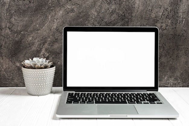 An open laptop with blank white screen on wooden desk against black wall