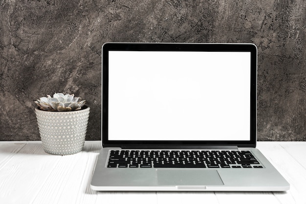 검은 벽에 나무 책상에 빈 흰색 화면이 열려있는 노트북