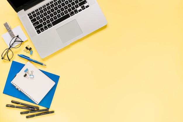 Открытый ноутбук с офисными канцелярскими принадлежностями на желтом фоне