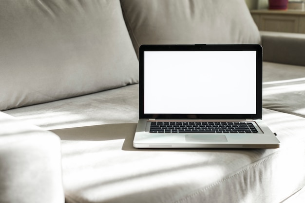 An open laptop with white display screen on gray sofa