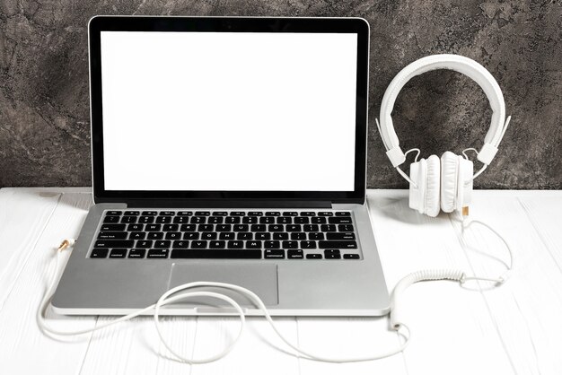 An open laptop with white headphone on desk against concrete wall