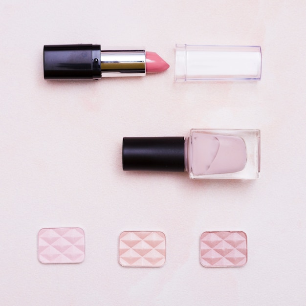 An open lipstick; nail varnish bottle and eyeshadow on pink background
