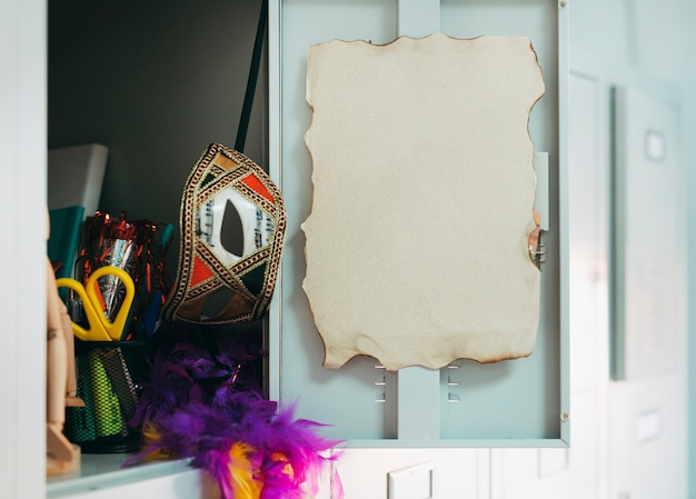 Open locker door with burnt page; carnival mask; scissor and feather boa