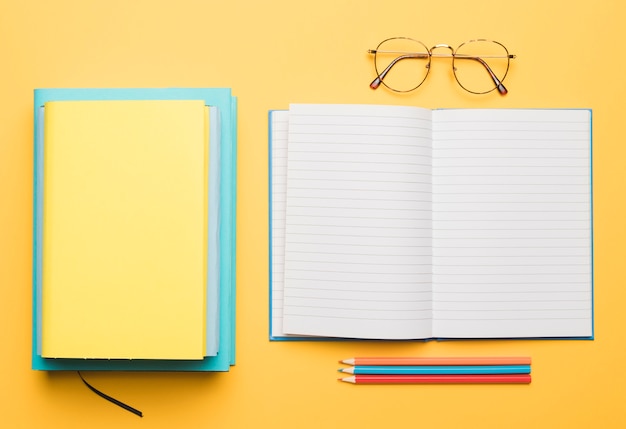 Open notebook and stack of textbooks next to glasses and set of pencils