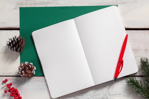 open notebook on the wooden table with a pen and Christmas decorations.