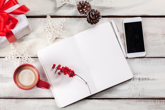 The open notebook on the wooden table with a phone and Christmas decorations.