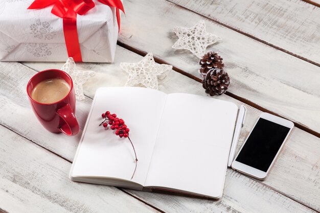 open notebook on the wooden table with a phone and Christmas decorations.