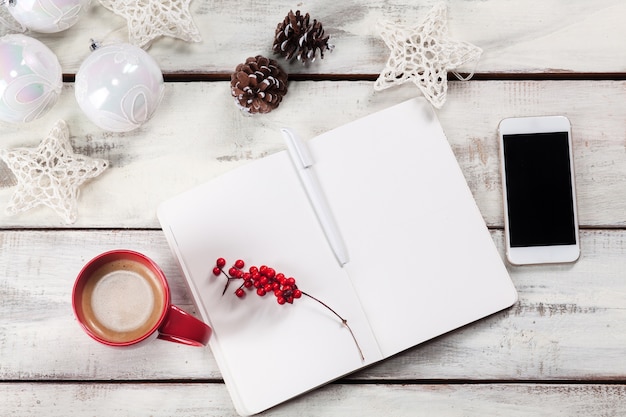 Free photo open notebook on wooden table with a phone and christmas decorations