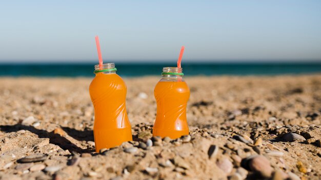 An open plastic juice bottle with red drinking straw in sand at beach