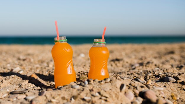 ビーチで砂の中の赤いストローで開いているプラスチックジュースの瓶