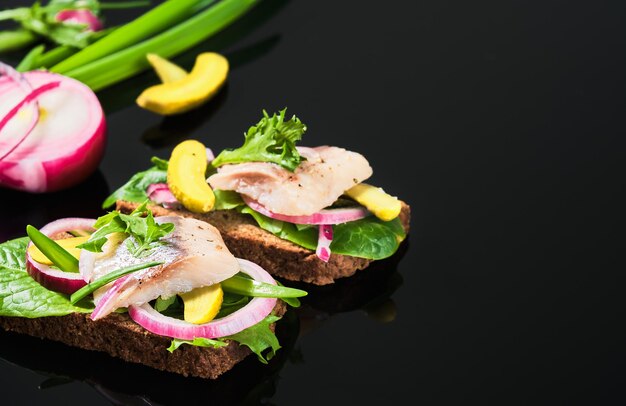 Open sandwich with dark rye bread, marinated matias herring, pickled cucumber and red onion on tha dark mirror table. Danish smorrebrod, selective focus and copy space