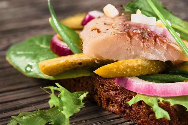 Open sandwich with young herring, herbs and pickled cucumber, close-up, selective focus. Traditional Danish smorrebrod. Sandwiches with matias herring arranged on a wooden background