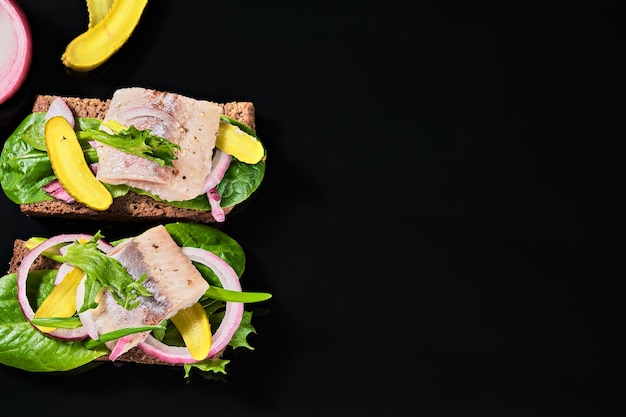 Open sandwich with young herring is a traditional Danish smorrebrod. Sandwiches with matias herring are located on a dark background with copy space. top view