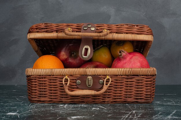 Открытый чемодан, полный фруктов на мраморном столе.