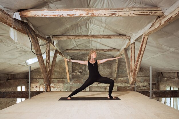 Open to world. A young athletic woman exercises yoga on an abandoned construction building. Mental, physical health balance. Concept of healthy lifestyle, sport, activity, weight loss, concentration.