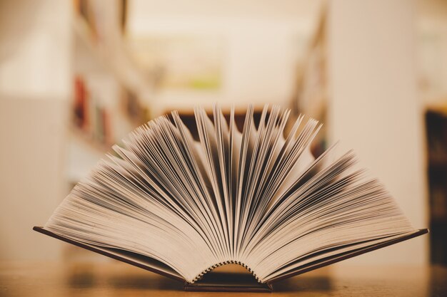 Opened book on the desk and isle of bookshelves in school study class room background 