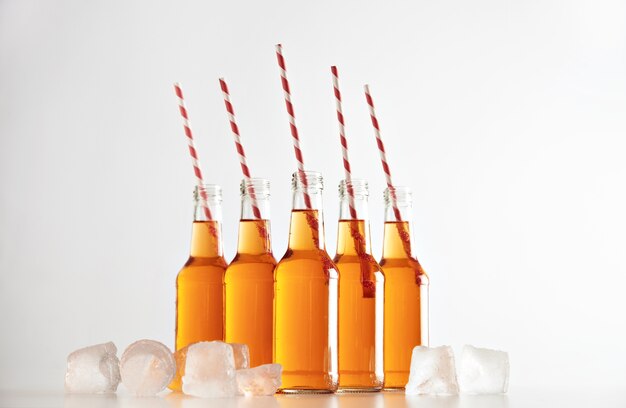 Opened bottles with cold lemonade inside and striped drink straws isolated on white in center between ice cubes