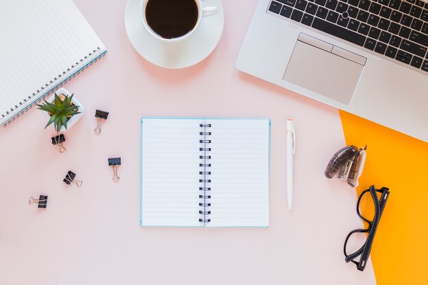 Opened notebook near coffee cup and glasses on pink desk with stationery