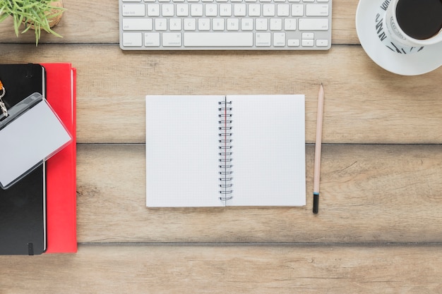 Opened notebook near stationery keyboard and coffee cup