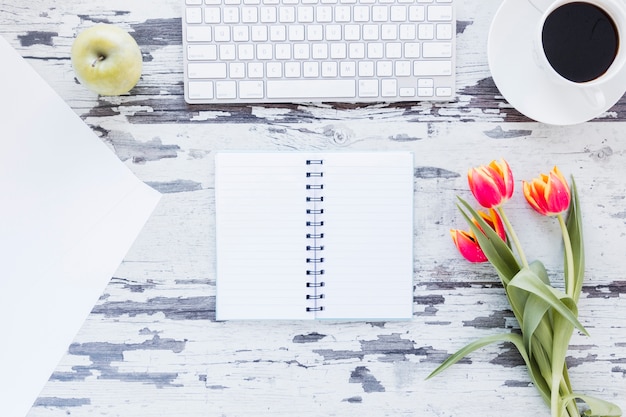 Opened notebook and tulip flowers near keyboard and coffee cup on shabby desk