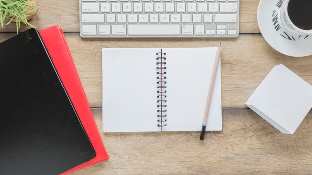 Opened notepad and stationery near keyboard and coffee cup