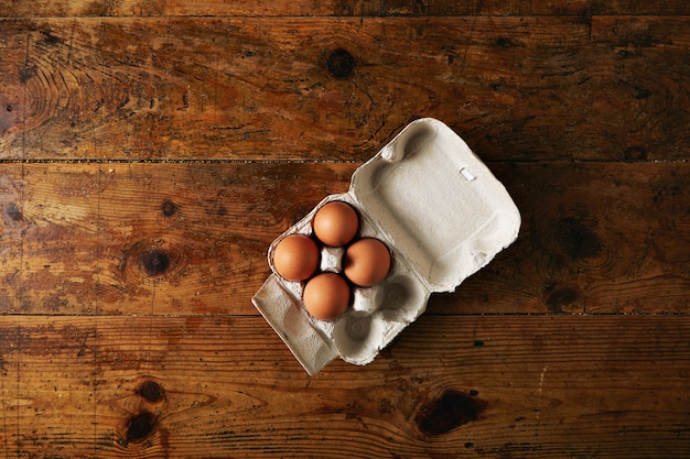 無料写真 粗い素朴な茶色の木製テーブルに4つの大きな茶色の卵を含む6つの卵のためのリサイクル可能な卵パックを開きました