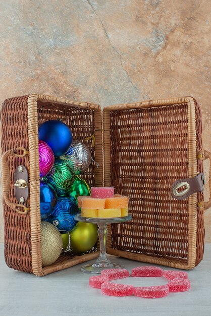 Открытый чемодан, полный красочных новогодних шаров и мармелада на мраморном фоне. Фото высокого качества