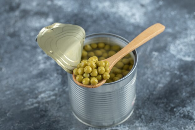 Opened tin green peas and wooden spoon.